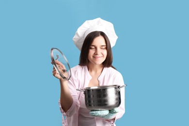 Happy young woman with cooking pot on light blue background