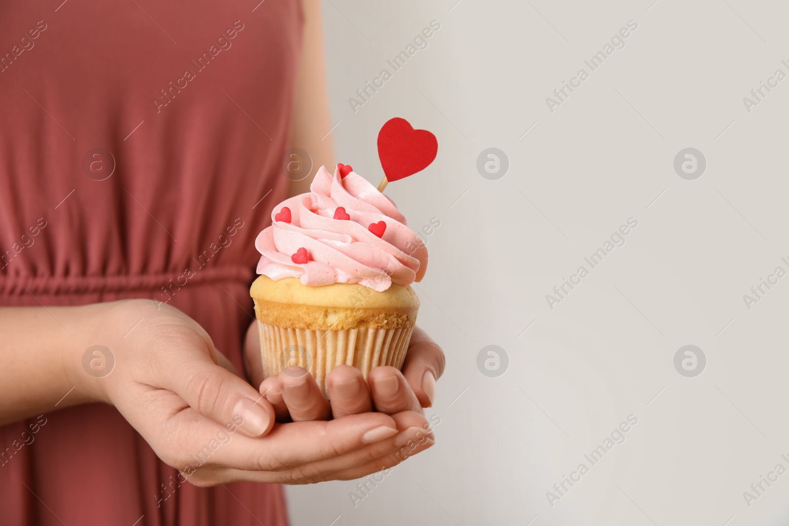Photo of Closeup view of woman holding tasty cupcake on light background, space for text. Valentine's Day celebration