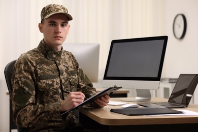 Photo of Military service. Young soldier with clipboard working at table in office