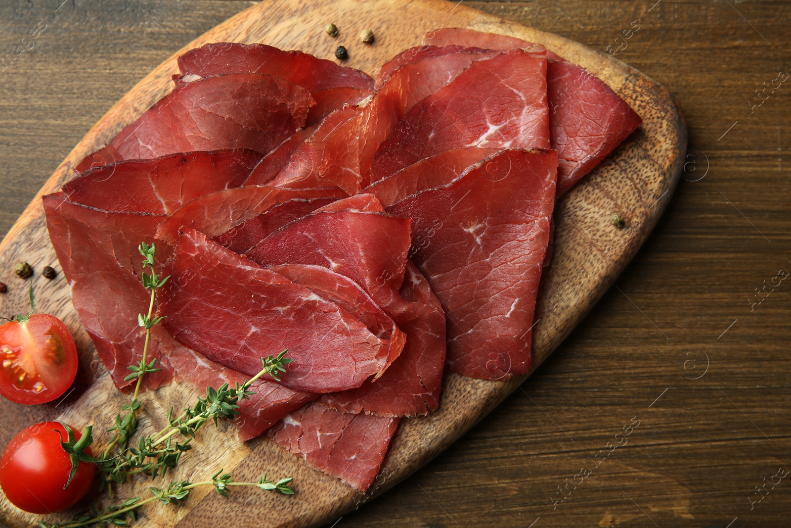 Photo of Tasty bresaola, peppercorns, tomatoes and thyme on wooden table, top view