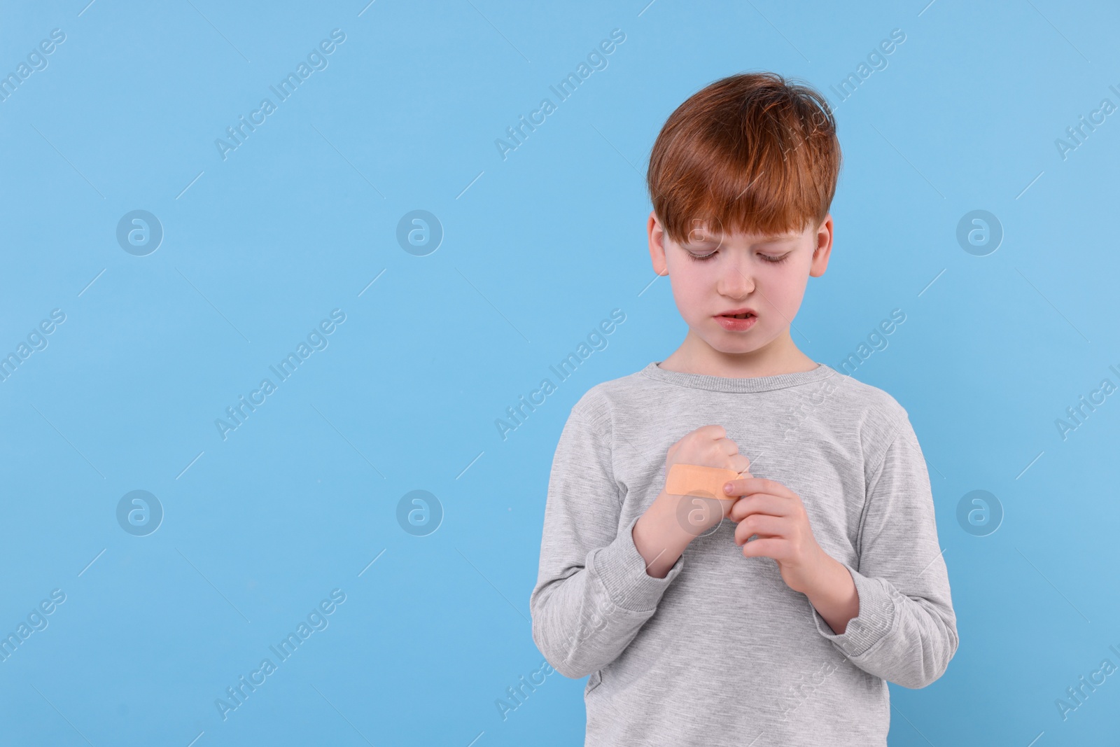 Photo of Little boy putting sticking plaster onto hand on light blue background. Space for text