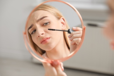 Young woman with eyelash loss problem applying mascara indoors