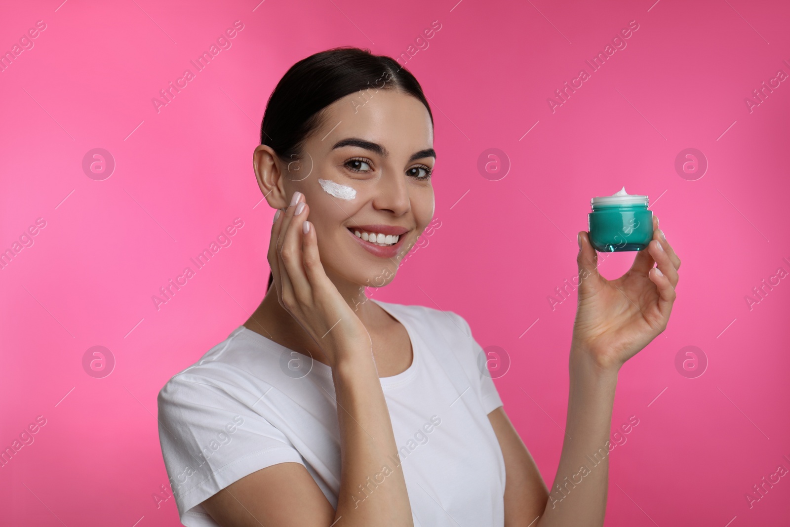 Photo of Young woman applying facial cream on pink background