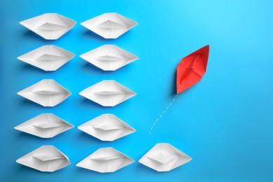 Photo of Red paper boat floating away from others on light blue background, flat lay. Uniqueness concept
