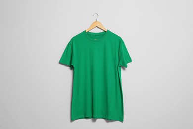 Photo of Hanger with green t-shirt on light wall. Mockup for design