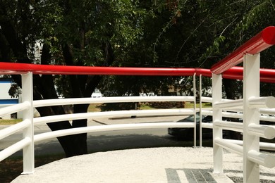 Ramp with red metal handrailings near trees outdoors