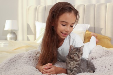 Cute little girl with kitten on white blanket at home. Childhood pet