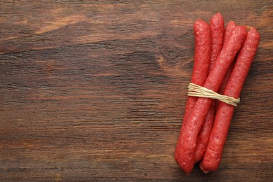 Photo of Many thin dry smoked sausages on wooden table, top view. Space for text