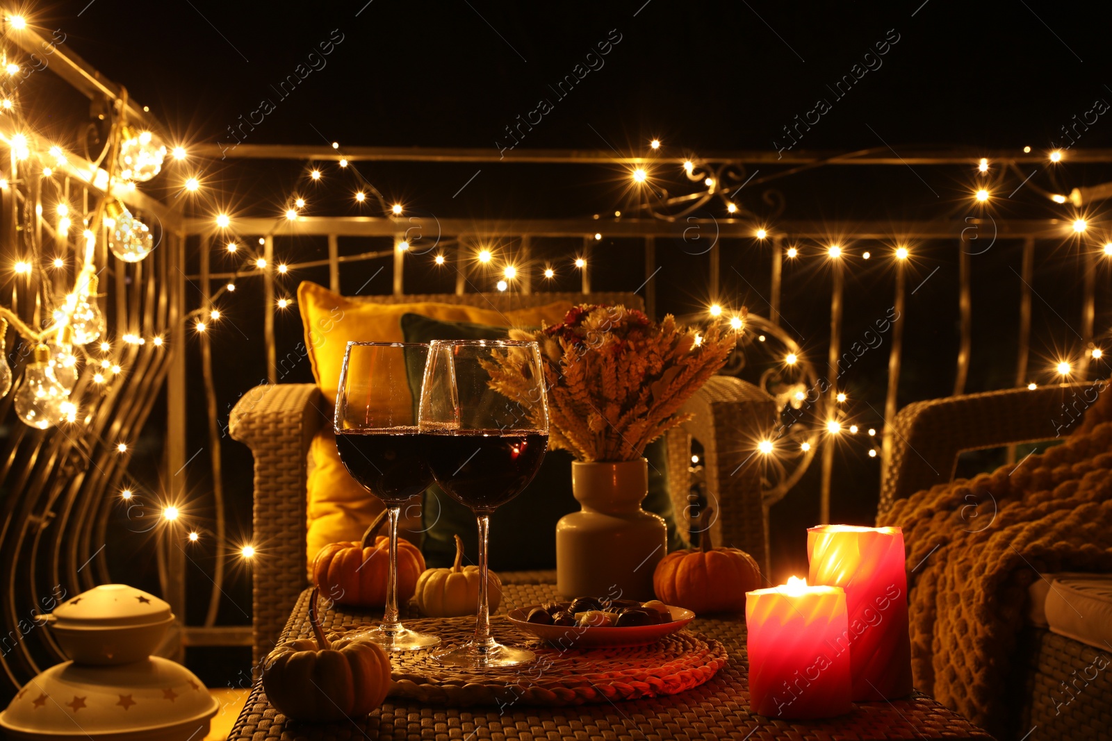 Photo of Glasses of wine, burning candles and decor on rattan table. Autumn evening on terrace