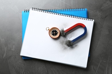 Photo of Notebooks, compass and magnet with iron powder on grey background, top view. Space for text