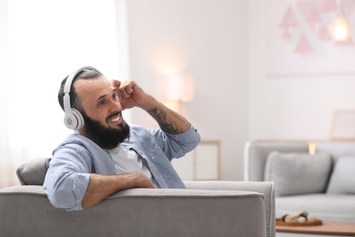 Mature man with headphones resting in armchair at home