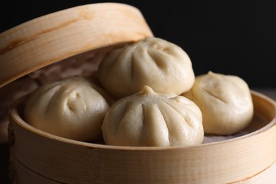 Delicious bao buns (baozi) in bamboo steamer on black background, closeup