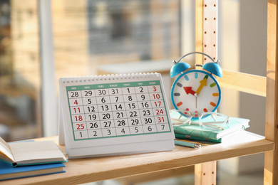 Paper calendar and alarm clock on wooden shelf indoors