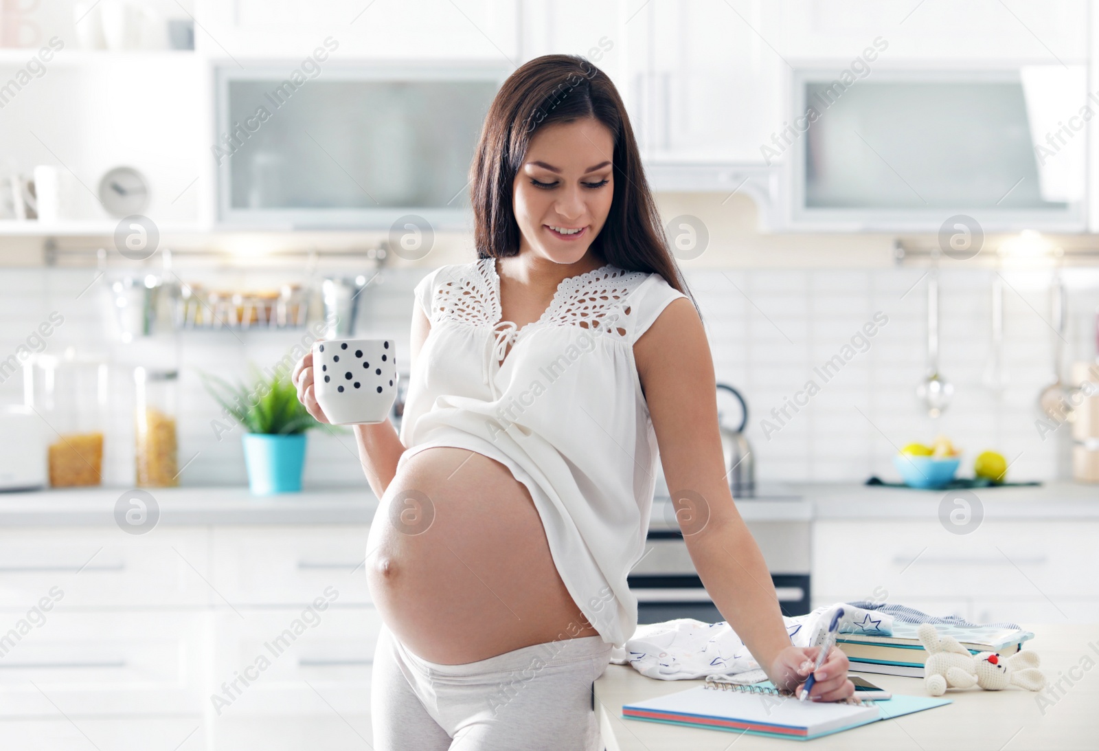 Photo of Pregnant woman writing packing list for maternity hospital in kitchen