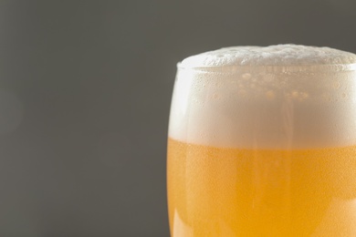 Glass of tasty beer with foam on color background, closeup