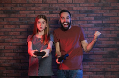 Photo of Young man and teenage girl playing video games with controllers near brick wall