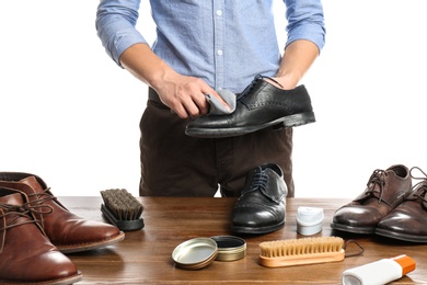 Man cleaning leather shoe at wooden table against white background, closeup