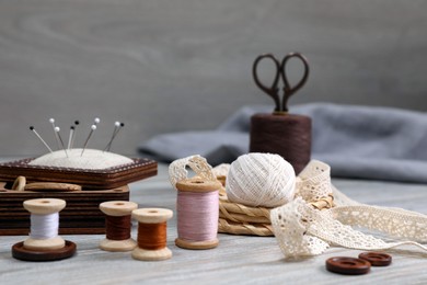 Photo of Color threads and different sewing accessories on white wooden table