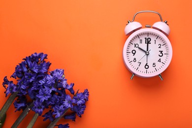 Photo of Pink alarm clock and beautiful hyacinth flowers on orange background, flat lay. Spring time
