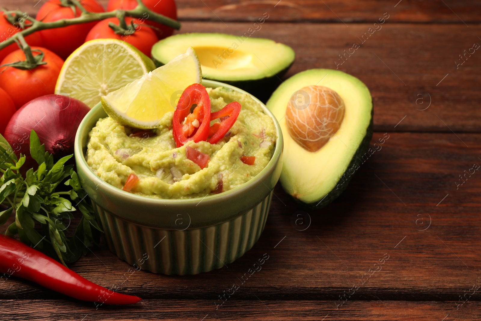 Photo of Bowl of delicious guacamole and ingredients on wooden table, closeup. Space for text