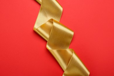 Photo of Beautiful golden ribbon on red background, top view