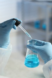 Scientist dripping liquid from pipette into beaker in laboratory, closeup