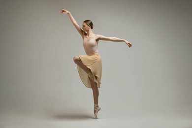 Photo of Young ballerina practicing dance moves on grey background