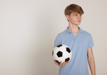 Teenage boy with soccer ball on light grey background. Space for text