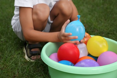 Photo of Little boy with basin of water bombs on green grass, closeup
