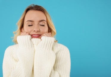 Beautiful woman in stylish warm sweater on light blue background. Space for text