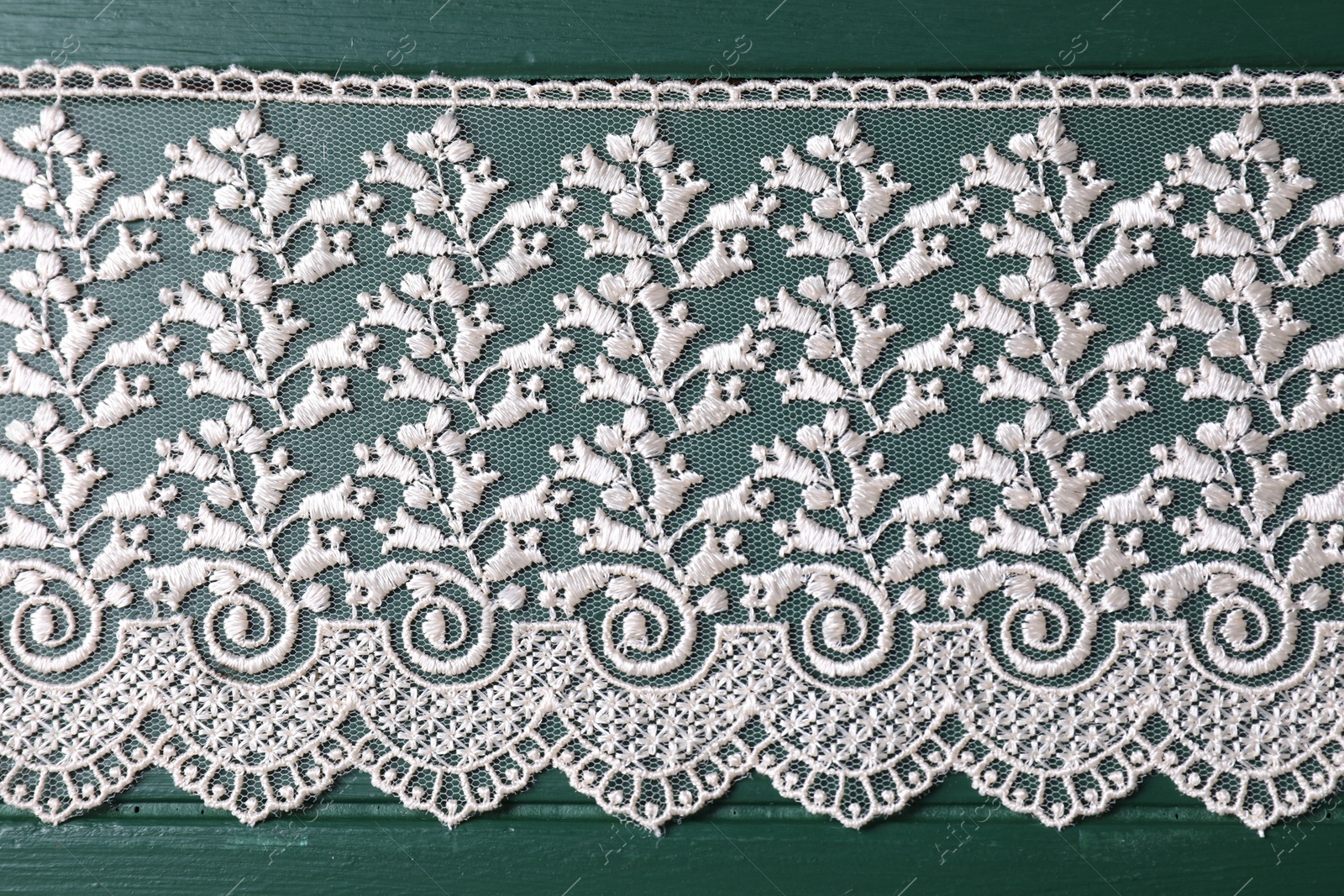 Photo of Beige lace on green wooden table, top view