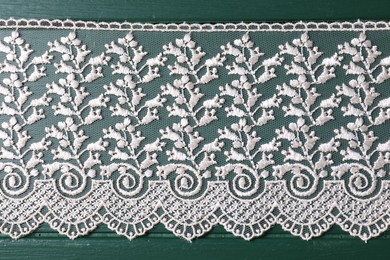 Beige lace on green wooden table, top view