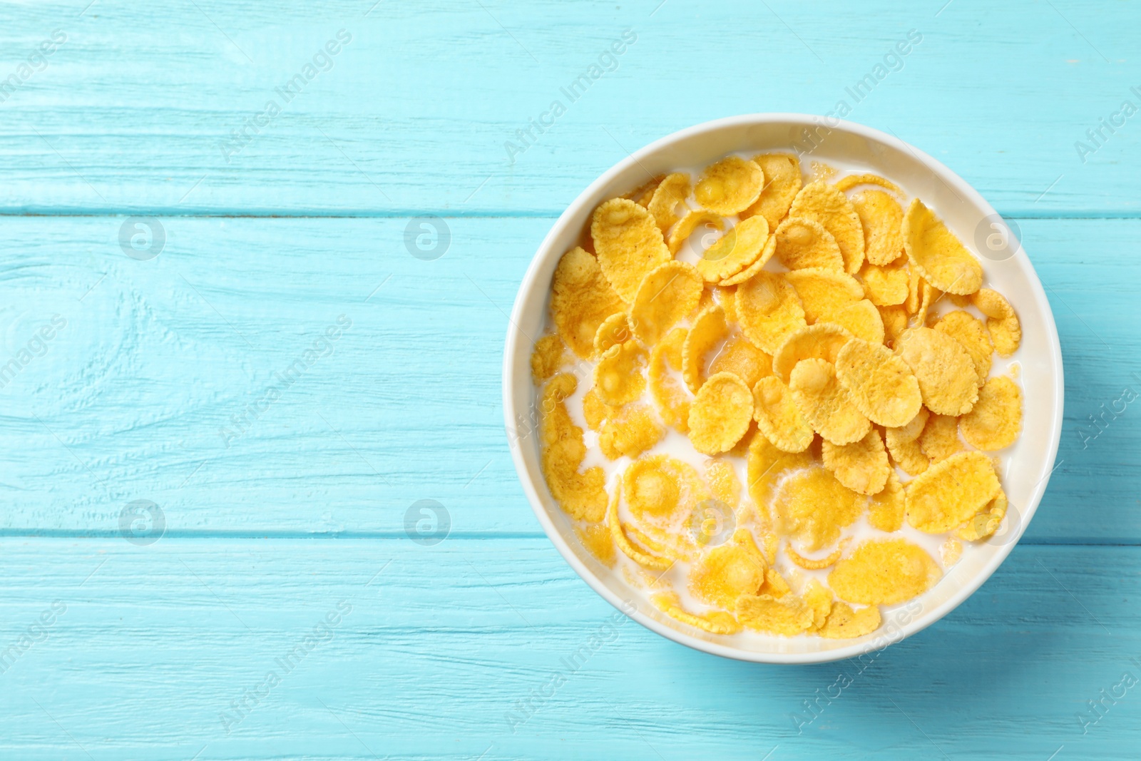 Photo of Tasty crispy corn flakes with milk on light blue wooden  table, top view. Space for text