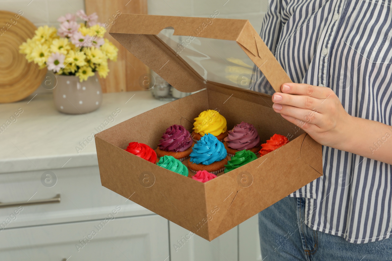 Photo of Woman holding box with delicious colorful cupcakes indoors, closeup