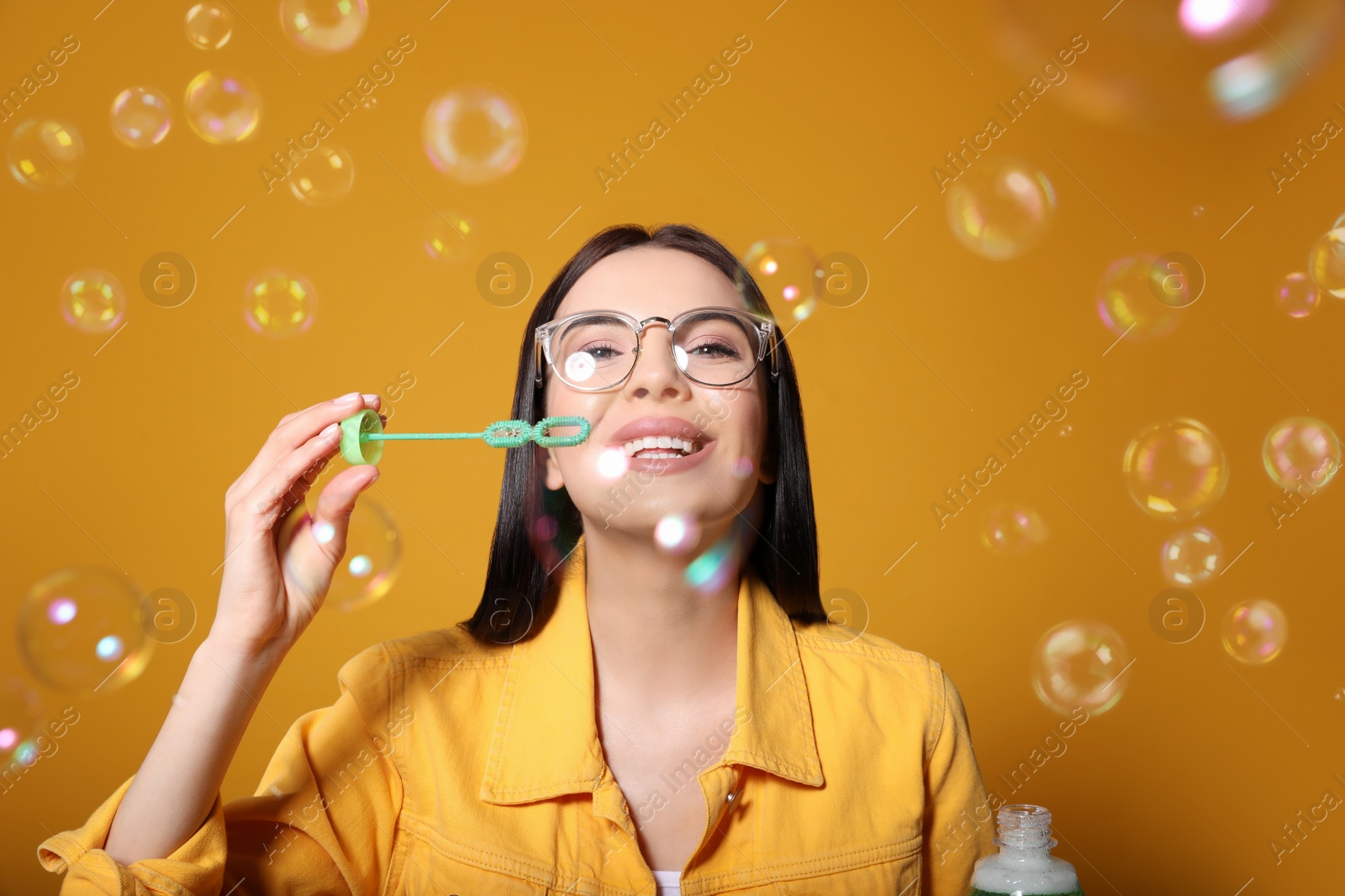 Photo of Young woman blowing soap bubbles on yellow background