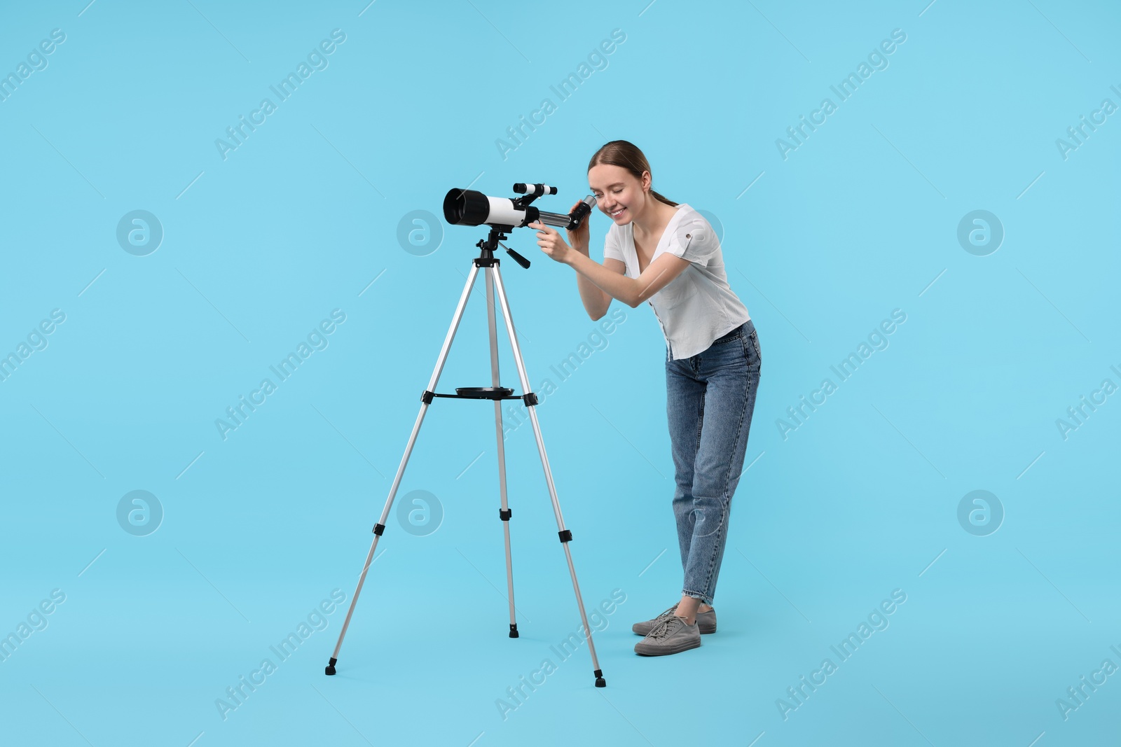 Photo of Young astronomer looking at stars through telescope on light blue background