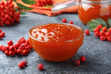 Delicious rowan jam in glass bowl and berries on grey table, closeup