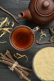 Photo of Aromatic licorice tea in cup, teapot, dried sticks of licorice root and powder on black wooden table, flat lay