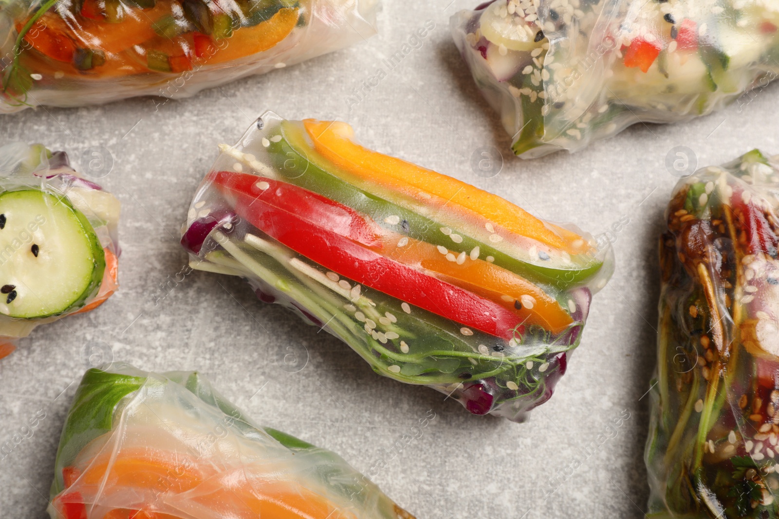 Photo of Many different delicious rolls wrapped in rice paper on grey table, flat lay