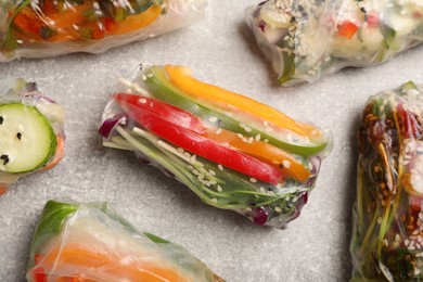 Many different delicious rolls wrapped in rice paper on grey table, flat lay