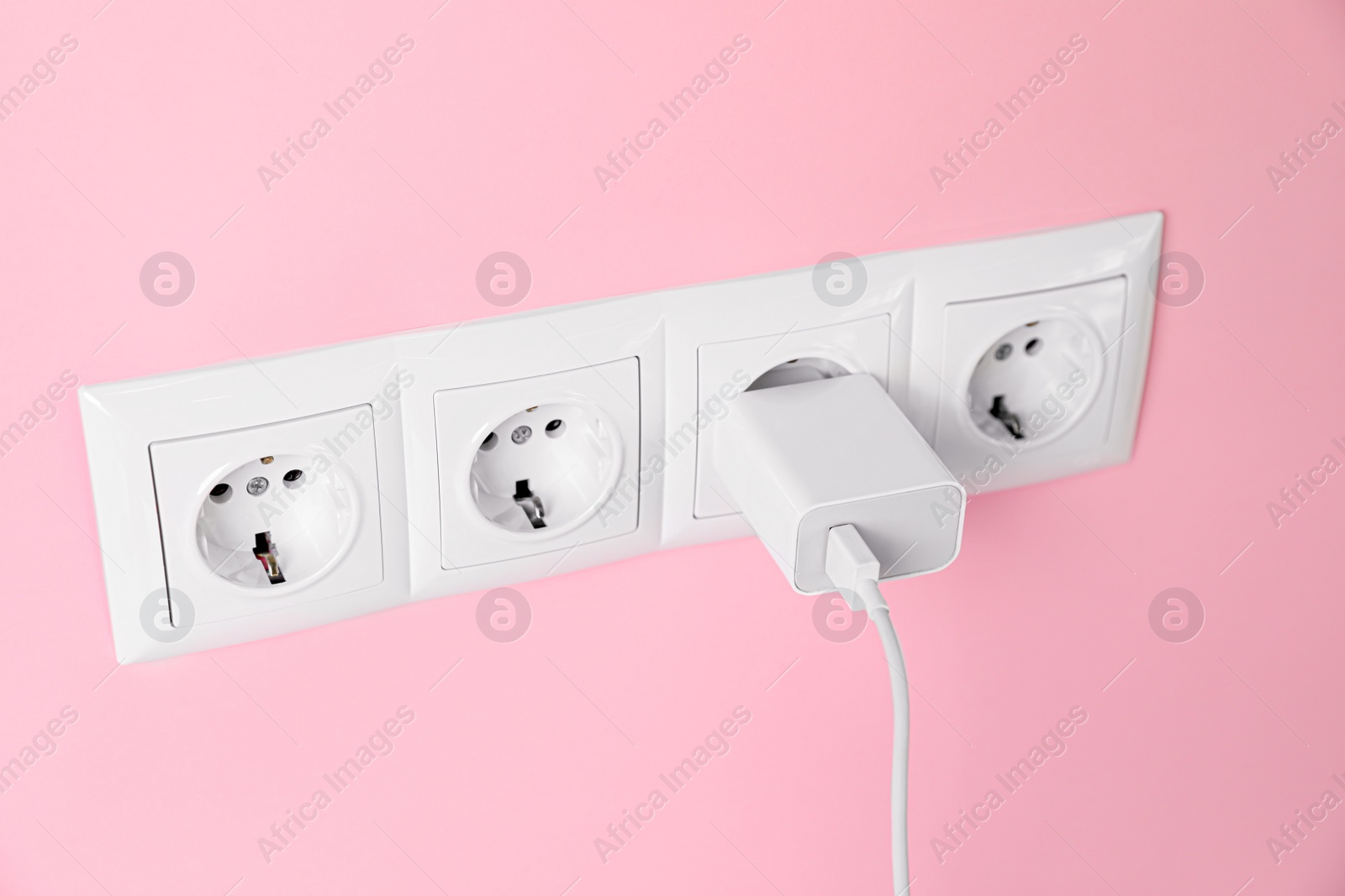 Photo of Charger adapter plugged into power sockets on pink wall. Electrical supply