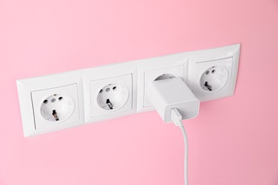 Charger adapter plugged into power sockets on pink wall. Electrical supply