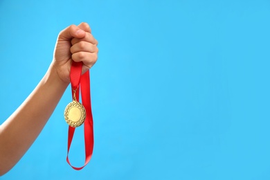 Photo of Woman holding gold medal on light blue background, closeup. Space for text