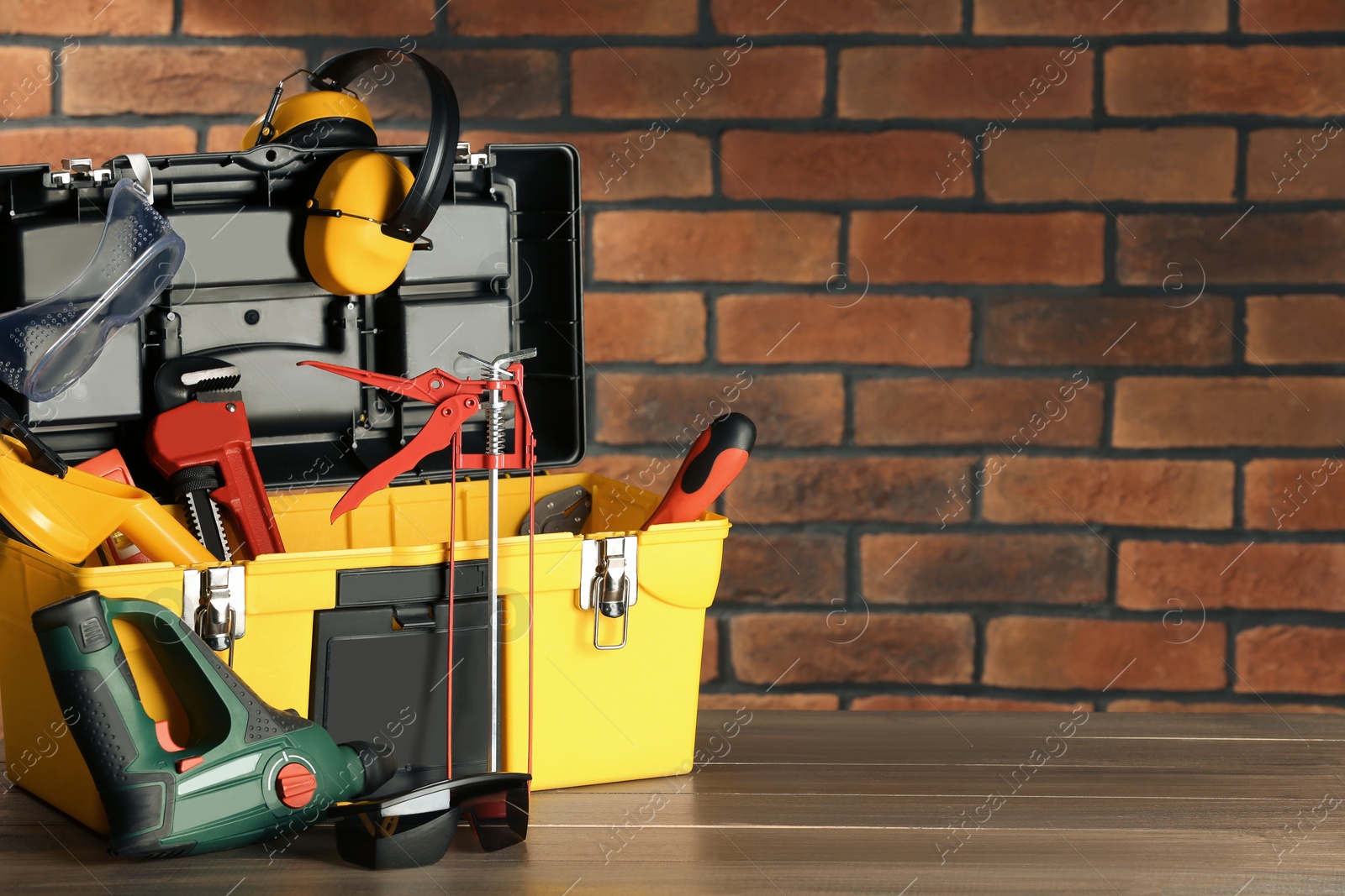 Photo of Box with different tools for repair on wooden table near brick wall, space for text