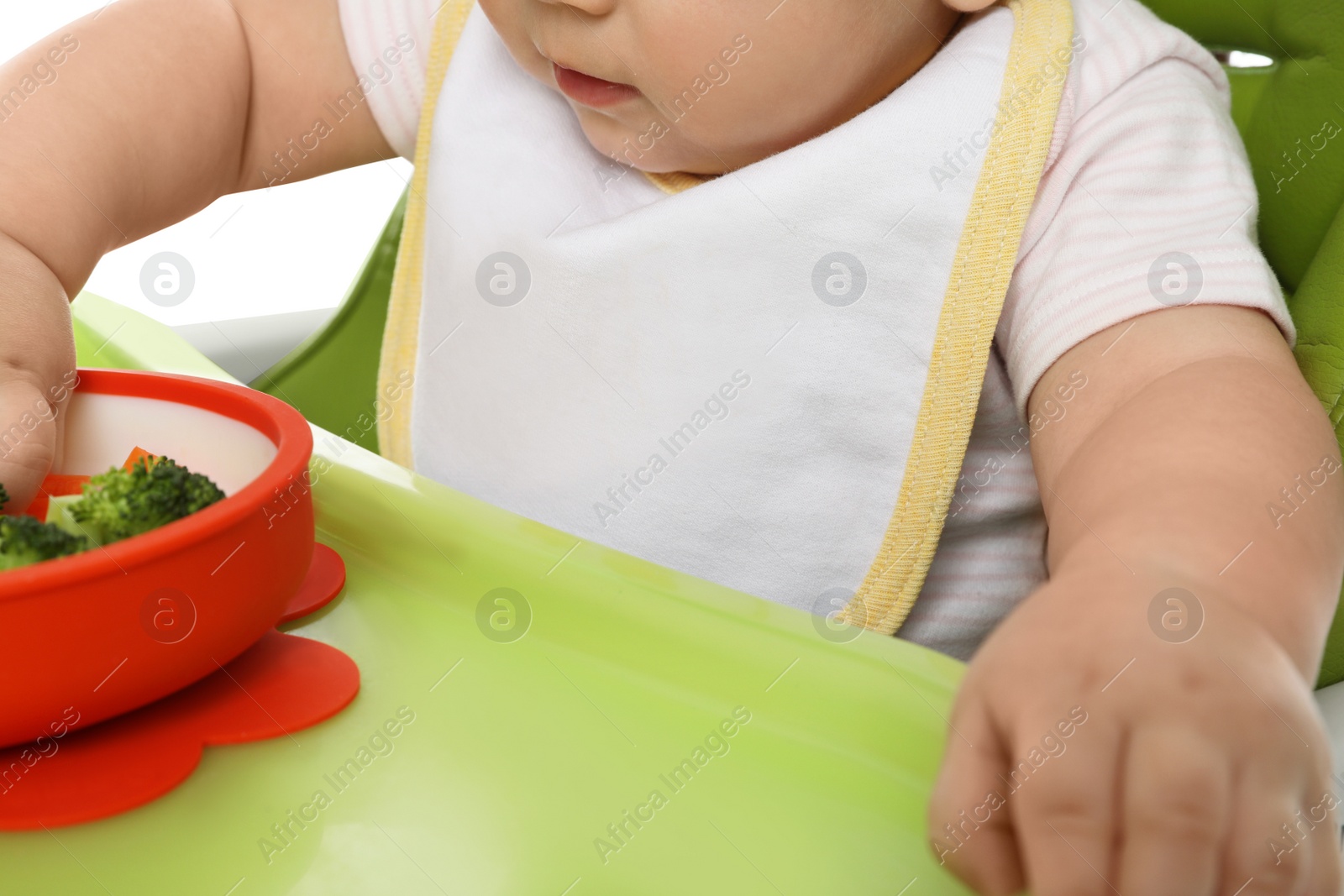 Photo of Cute little baby wearing bib while eating on white background, closeup