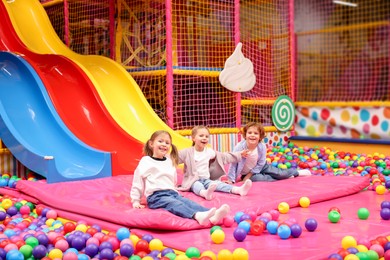 Photo of Happy kids playing in play room with slides, mats and ball pit