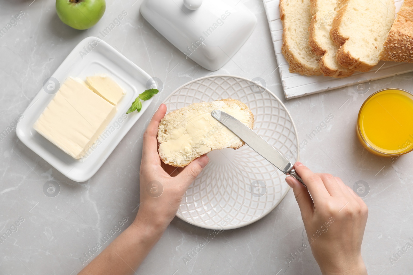 Photo of Woman spreading butter on slice of bread over table, closeup