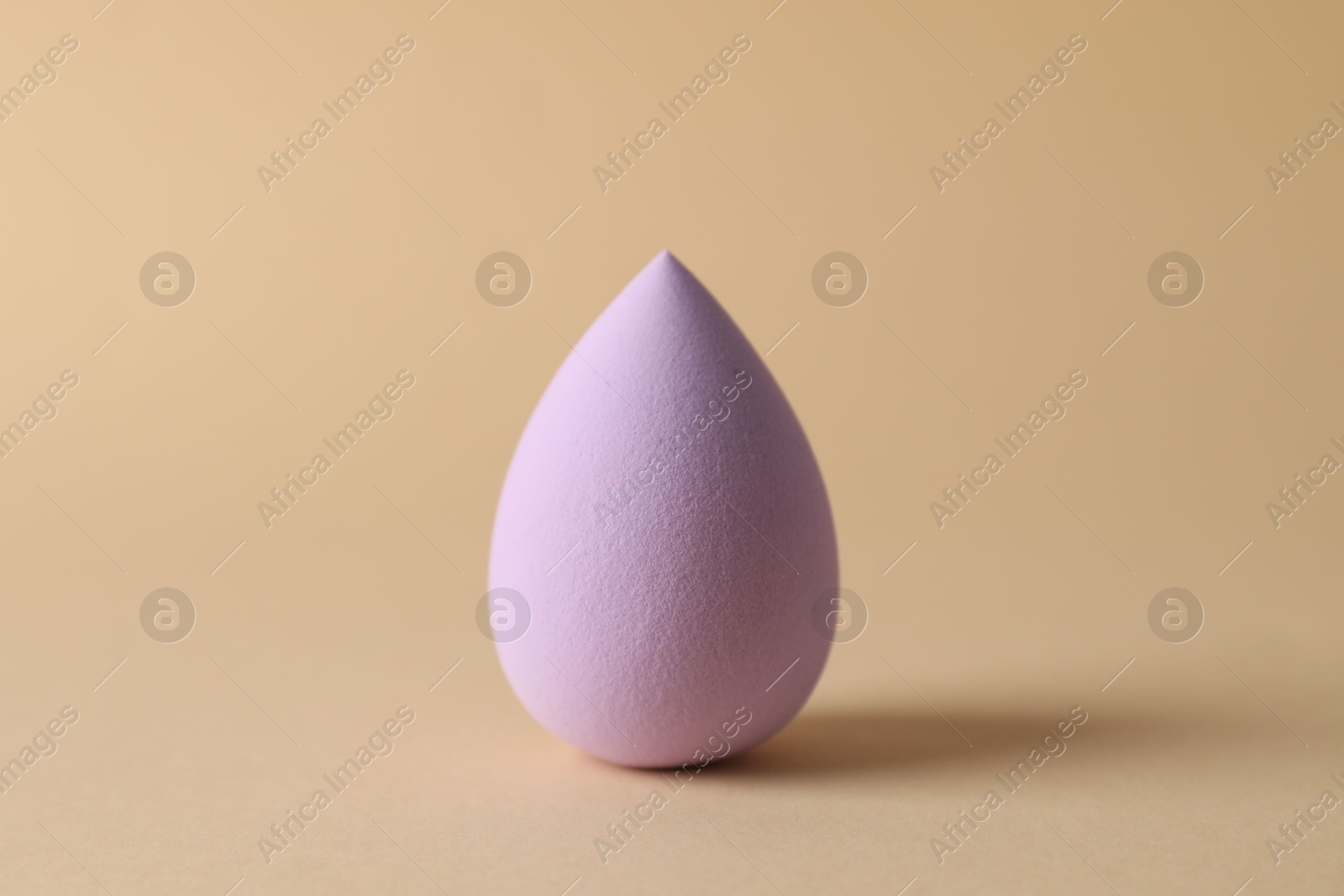 Photo of One violet makeup sponge on beige background