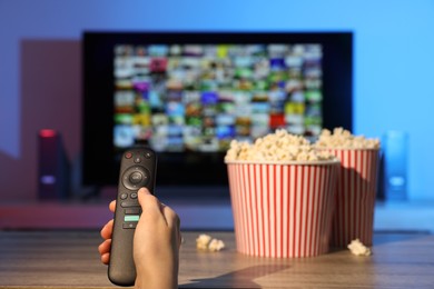 Woman switching channels on TV set with remote control at home, closeup