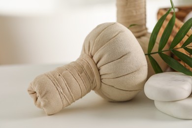 Photo of Spa composition. Herbal bags, stones and palm leaves on white table, closeup